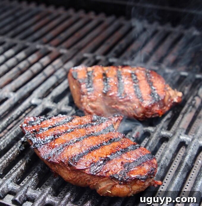 Two prime sirloin steaks sizzling on the hot grill grates, ready for a perfect sear.