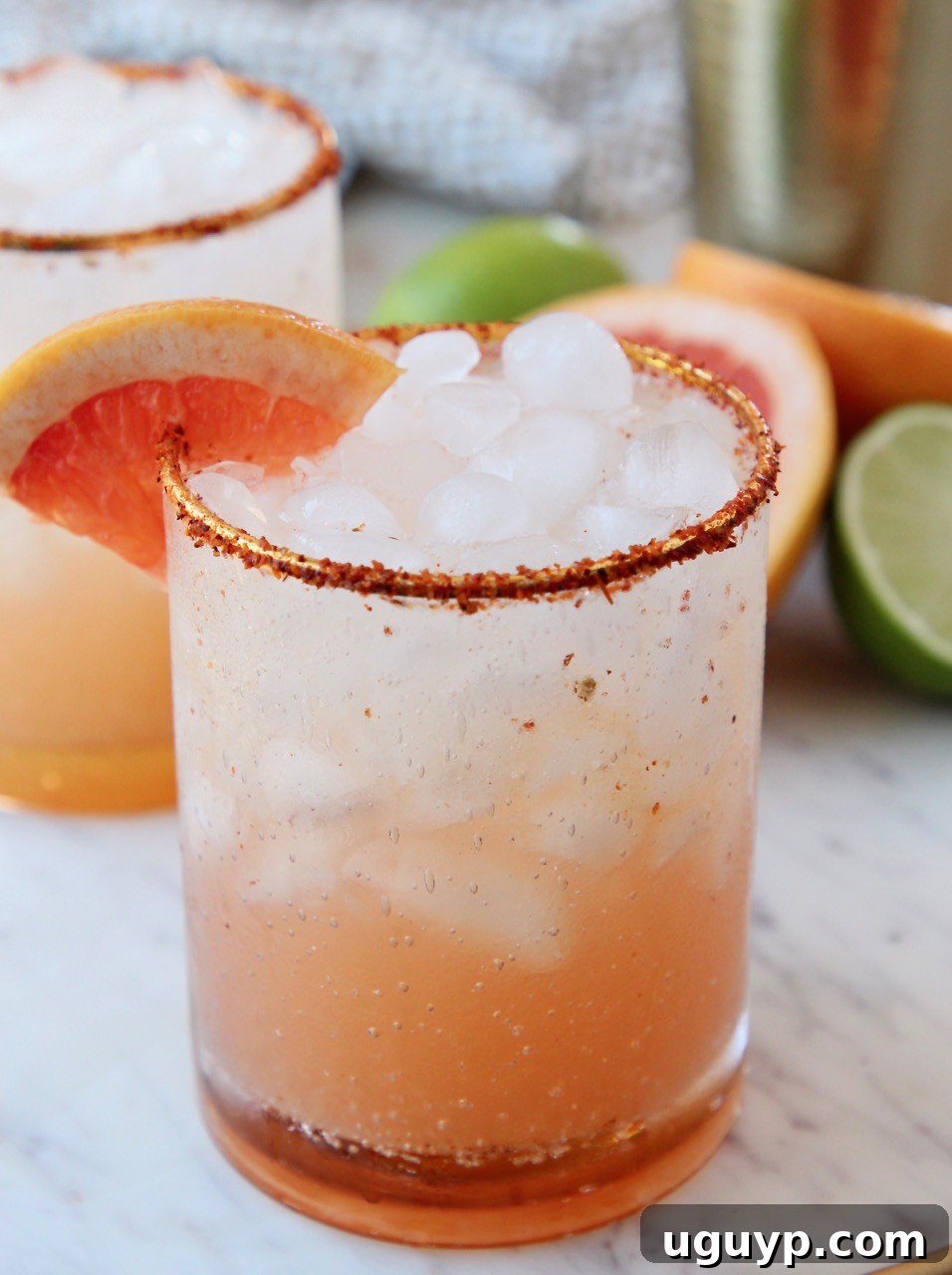 A refreshing Paloma cocktail in a glass, rimmed with Tajin and garnished with a grapefruit wedge, set against a bright background.