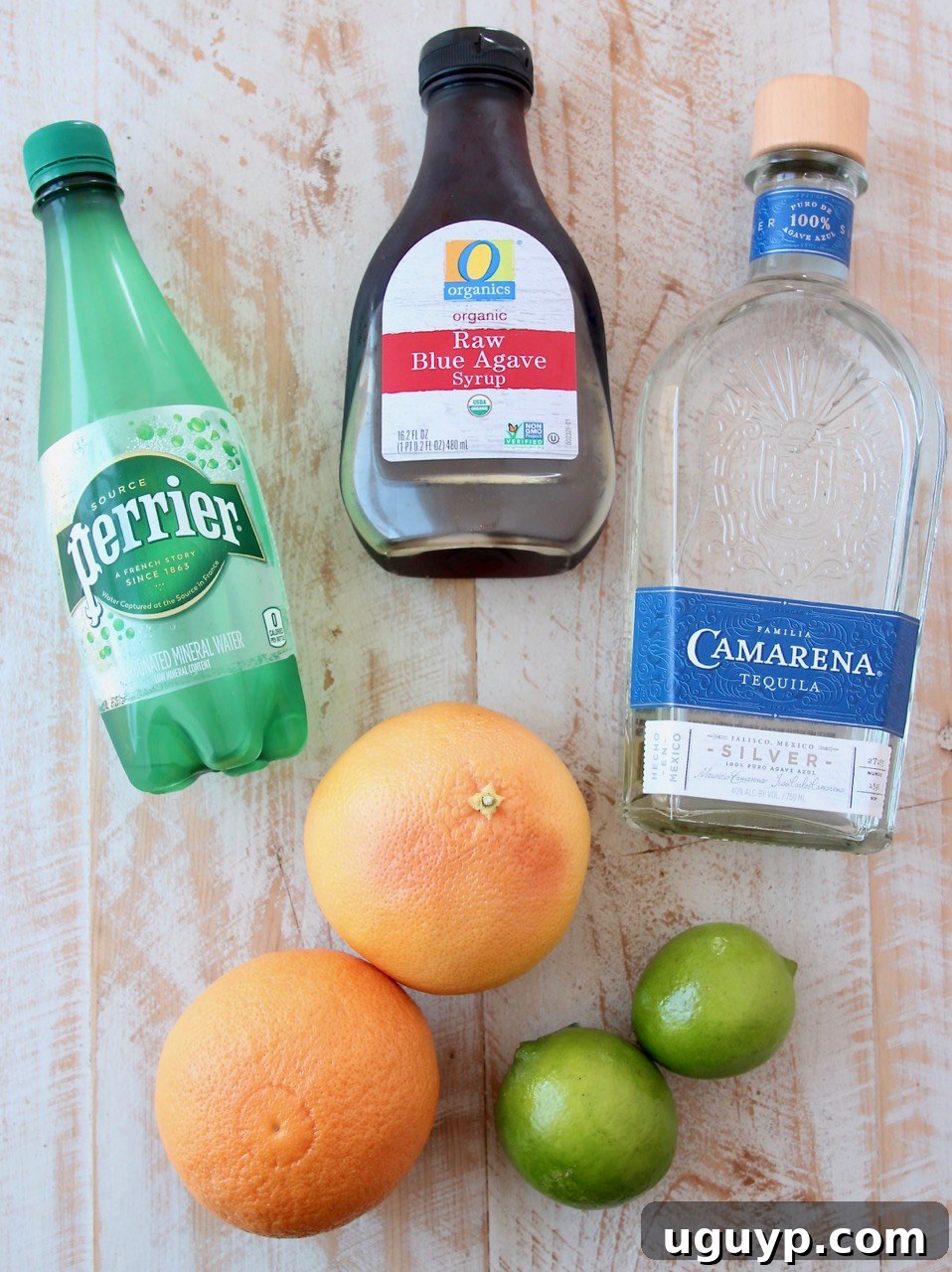 Various ingredients for a Paloma cocktail laid out on a surface, including tequila, grapefruit, lime, and agave nectar.