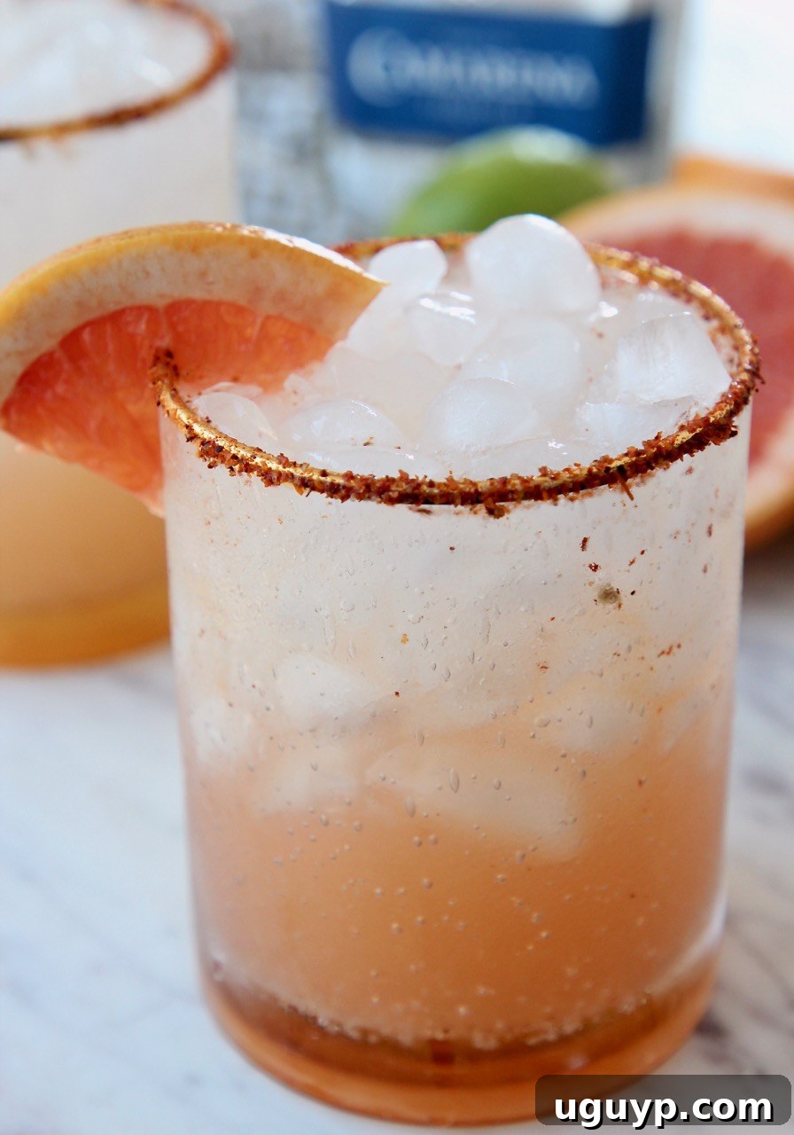 A close-up of a Paloma cocktail in a glass with a Tajin-rimmed edge and a grapefruit wedge garnish.
