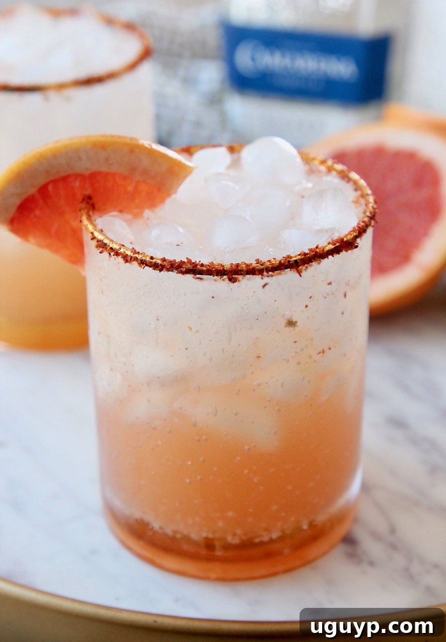 A Paloma cocktail in a glass with a Tajin rim and a vibrant grapefruit garnish.
