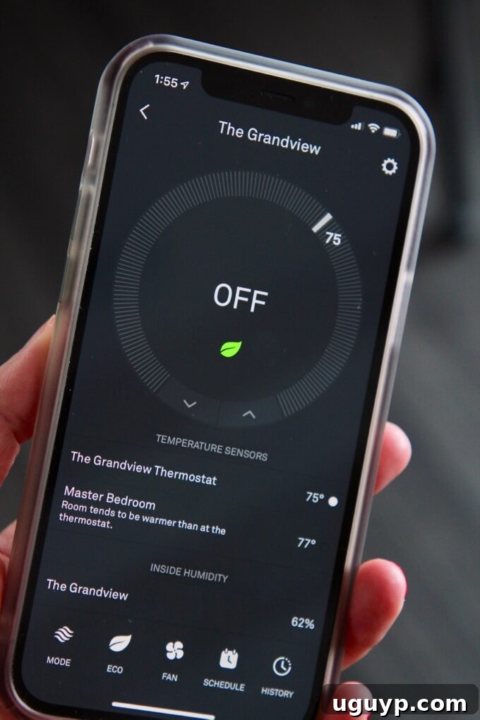 A hand holding an iPhone displaying the Nest app, showing smart home controls.