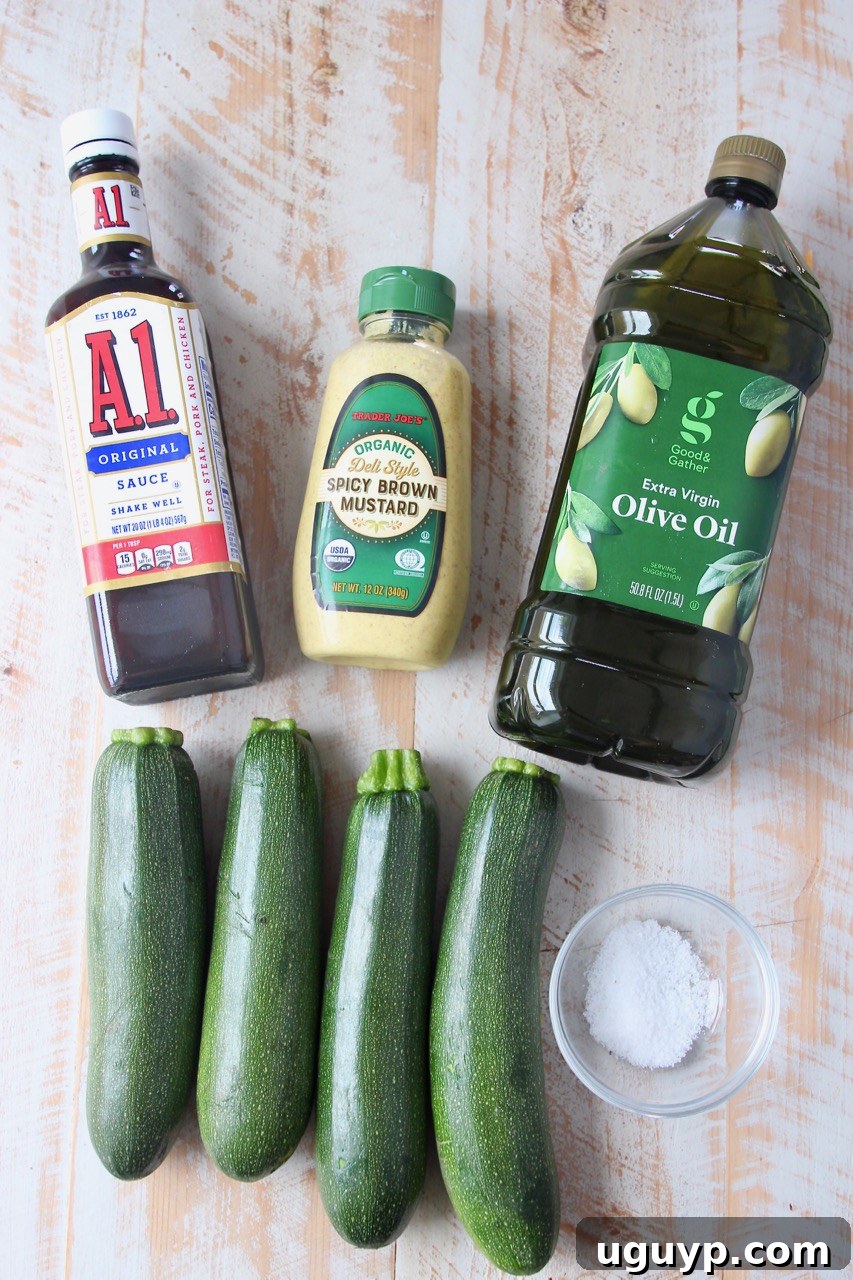A collection of fresh ingredients laid out for making marinated grilled zucchini: zucchini, spicy brown mustard, A1 sauce, olive oil, and sea salt.