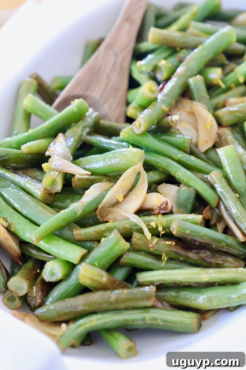 A serving bowl filled with perfectly cooked garlic green beans, garnished with fresh lemon slices, ready to be served.