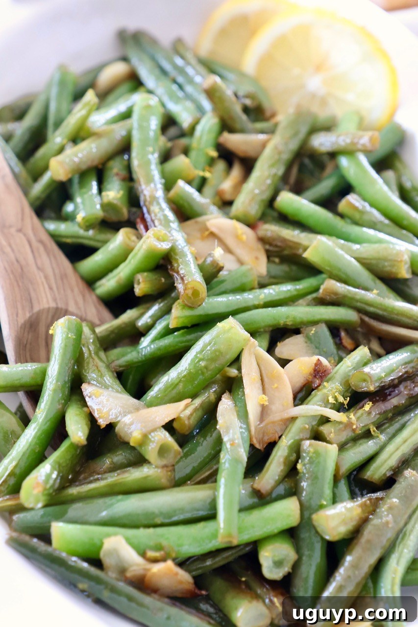 A close-up of cooked green beans arranged artfully in a white serving bowl, garnished with bright lemon slices, highlighting the fresh ingredients.