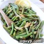 cooked green beans in white serving bowl with spoon