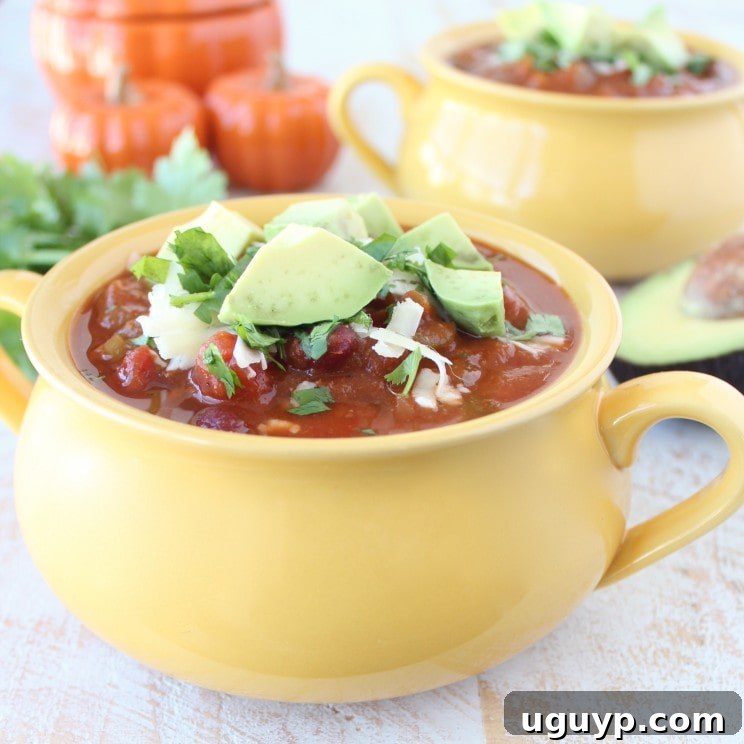 Yellow bowl filled with Pumpkin Chili garnished with melted cheese, avocado, and cilantro.