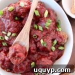 bbq meatballs in bowl with wooden spoon topped with diced green onions