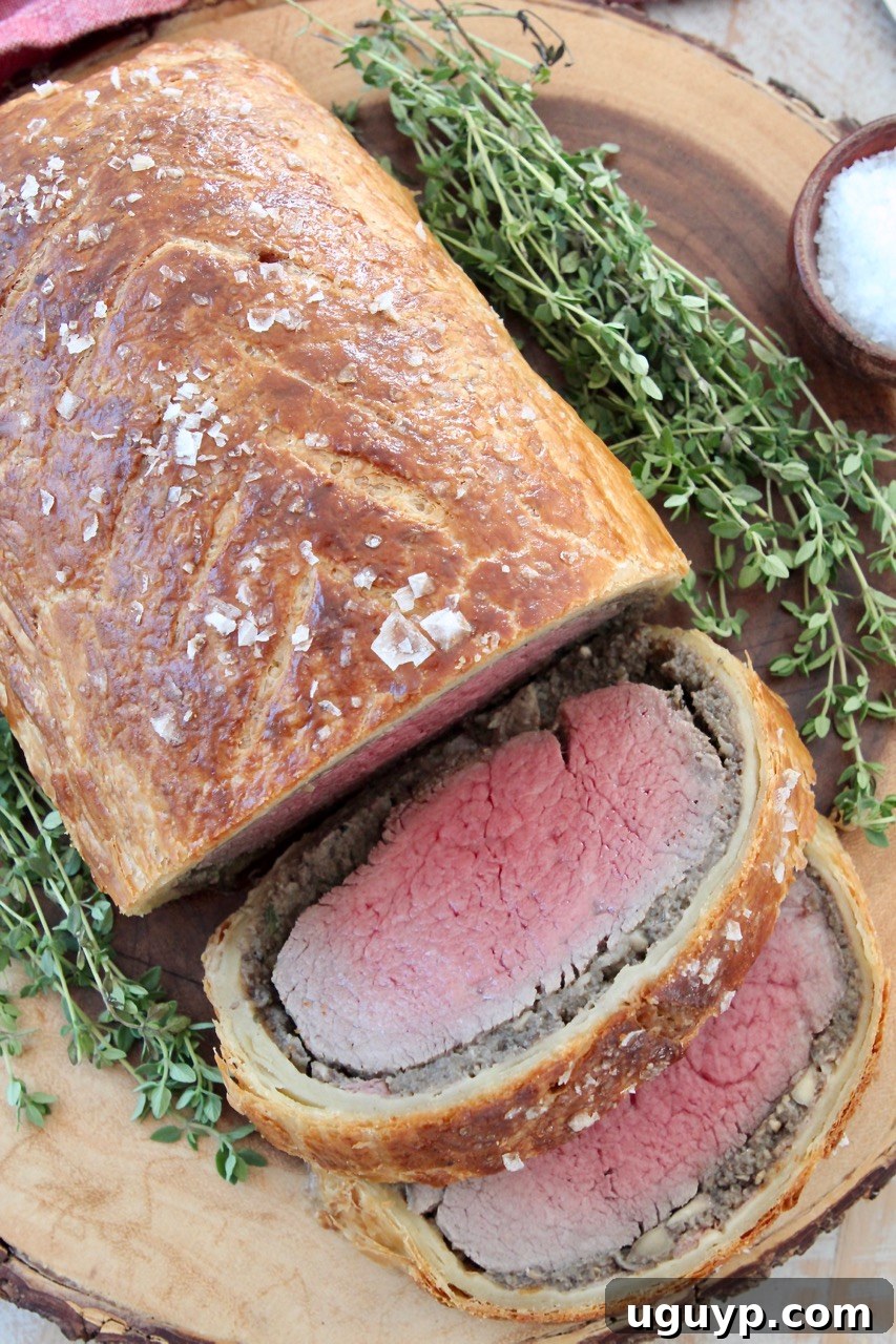 cooked, sliced beef wellington on wood serving tray with fresh herbs