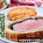 slice of beef wellington on place with mashed sweet potatoes and fresh herbs