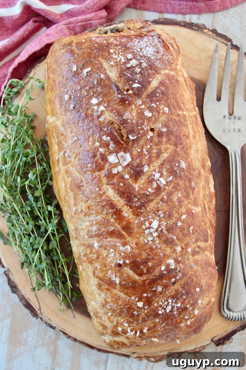 baked beef wellington on wood serving board with fresh herbs and serving fork