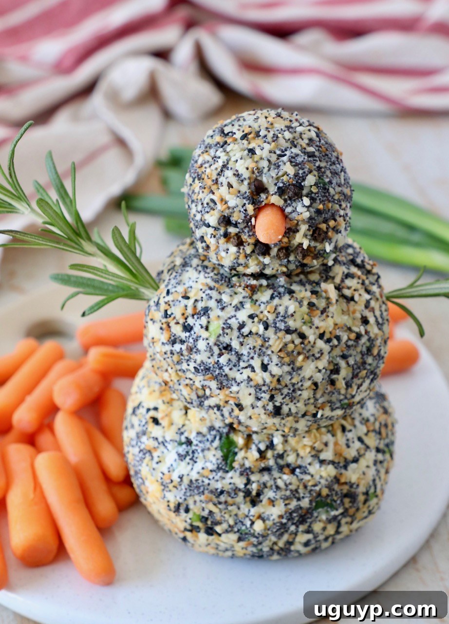 An adorable cheese ball snowman served on a platter with carrot stick arms and a festive presentation.