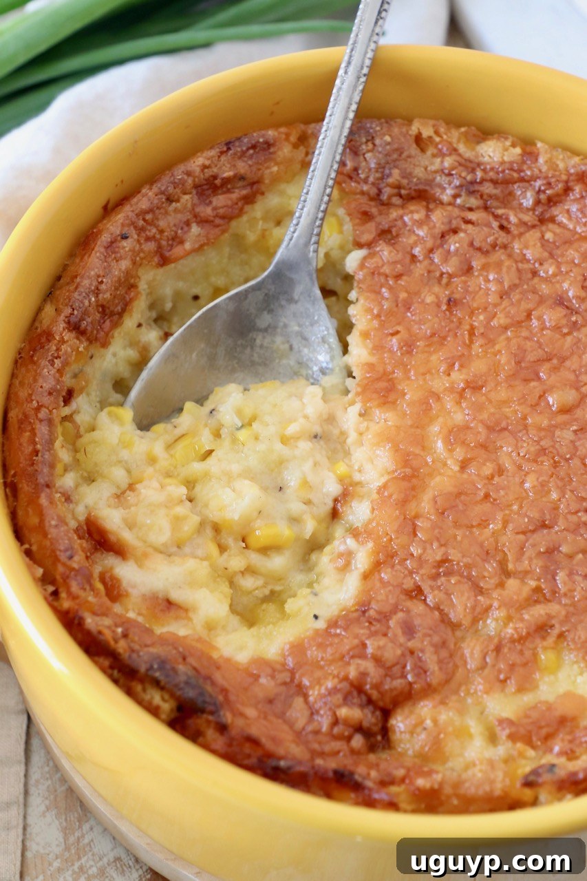 Close-up of a cheesy corn casserole in a yellow round baking dish with a serving spoon, highlighting the melted cheese topping.