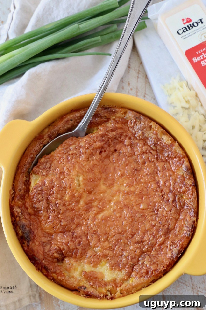 A generous portion of cheesy corn casserole in a yellow baking dish, with a serving spoon ready to scoop, illustrating its appealing texture.