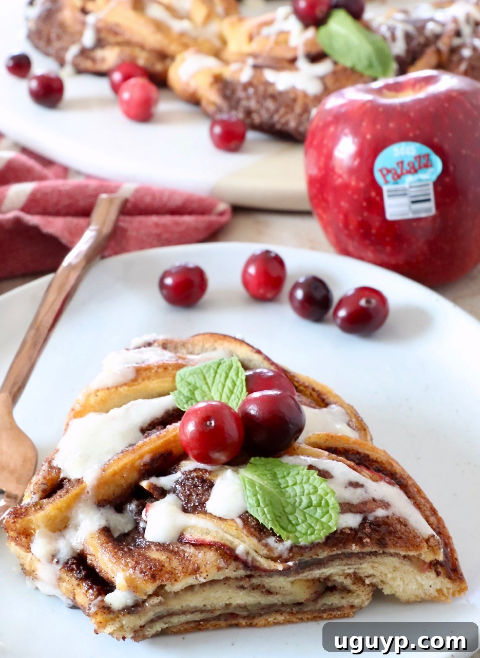 A delectable slice of apple cinnamon roll wreath on a white plate, adorned with a golden fork, ready to be enjoyed.