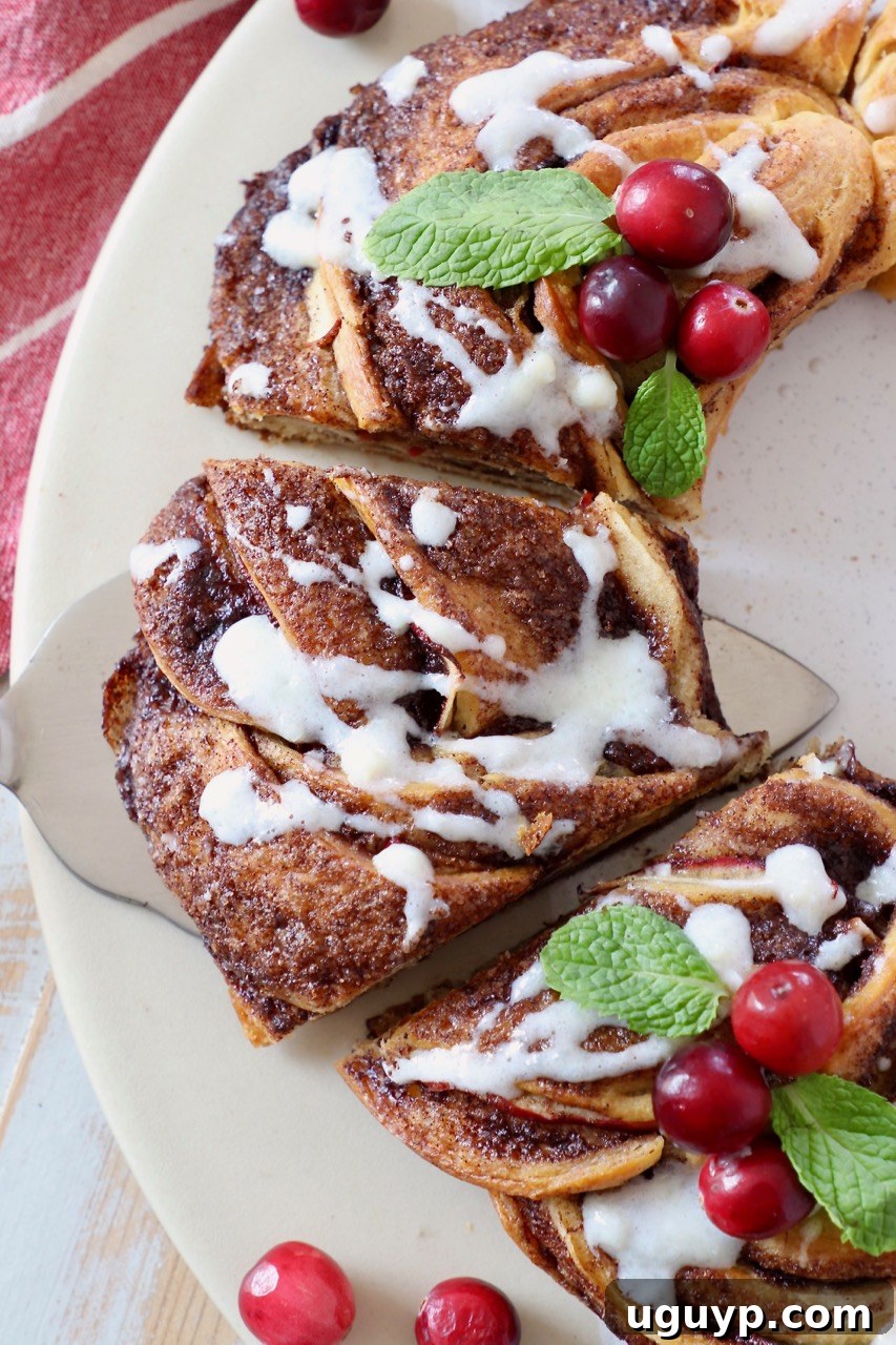 A baked apple cinnamon roll wreath generously drizzled with rich cream cheese frosting, on a simple white plate.