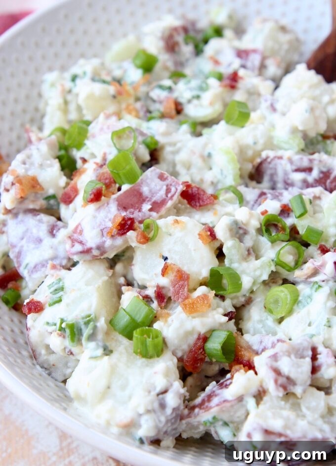 A creamy red potato salad in a white bowl, generously topped with fresh diced green onions.