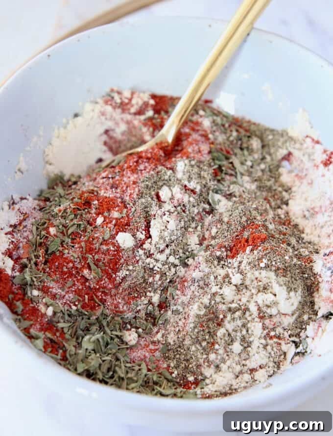 A bowl filled with a flavorful blend of mixed Cajun spices and herbs, with a gold spoon for serving.