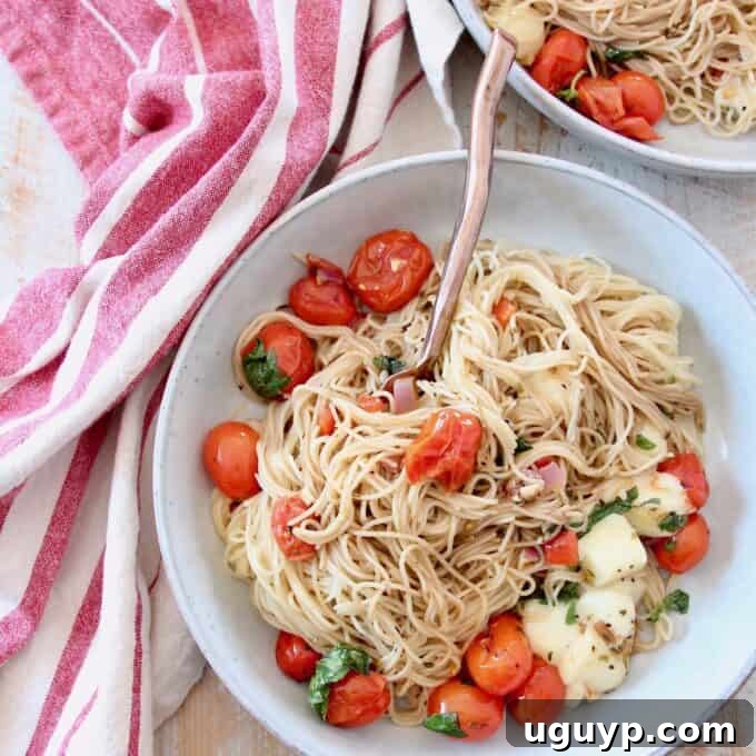 A bowl of cooked angel hair pasta tossed with fresh cherry tomatoes, vibrant basil leaves, and creamy mozzarella cheese.
