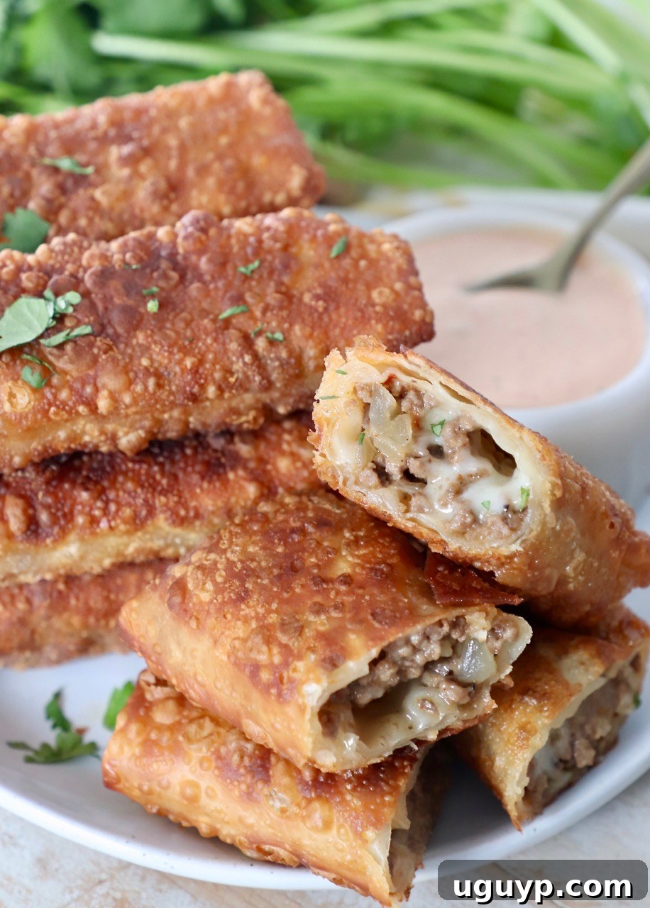 cheeseburger egg rolls stacked up on plate with side of thousand island dressing in white bowl
