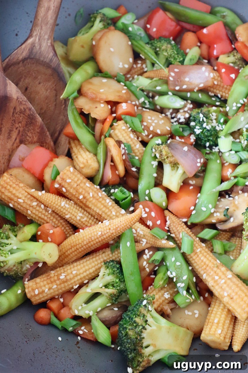 Close-up of stir fry vegetables cooking in a wok with a wooden spoon.