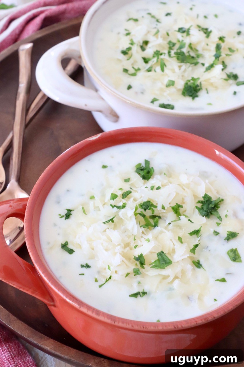 Two bowls of creamy and chunky potato soup, garnished with shredded Swiss cheese and fresh chopped parsley, on a wooden table.