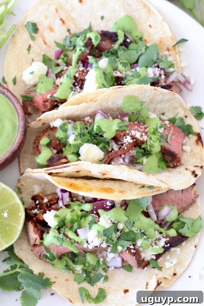 three steak tacos on plate topped with cilantro, sauce and cheese