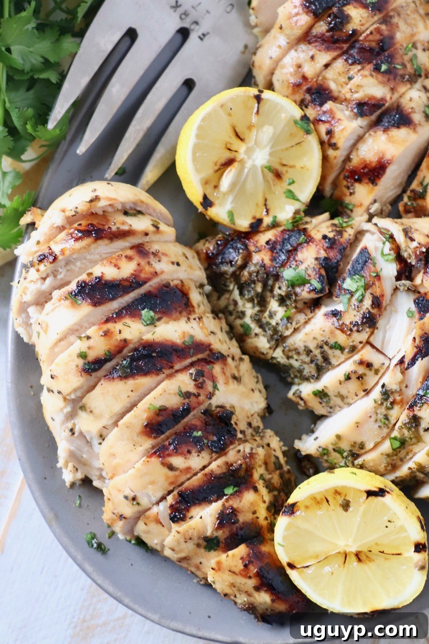 Perfectly sliced grilled Greek chicken breasts on a platter, garnished with fresh lemon slices and a fork, ready to be served.
