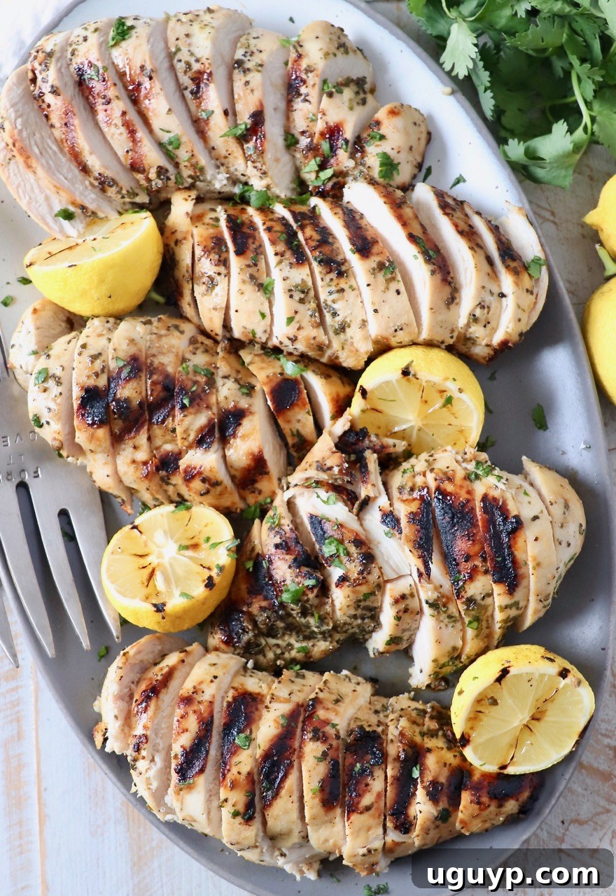 Beautifully sliced grilled Greek chicken breasts arranged artfully on a white plate, accompanied by fresh lemon wedges, ready to be enjoyed.
