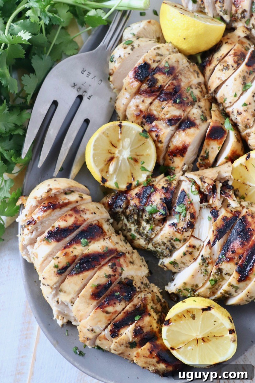 Grilled Greek chicken pieces artfully arranged on a plate, accompanied by perfectly grilled lemon halves, emphasizing the dish's zesty flavor profile.