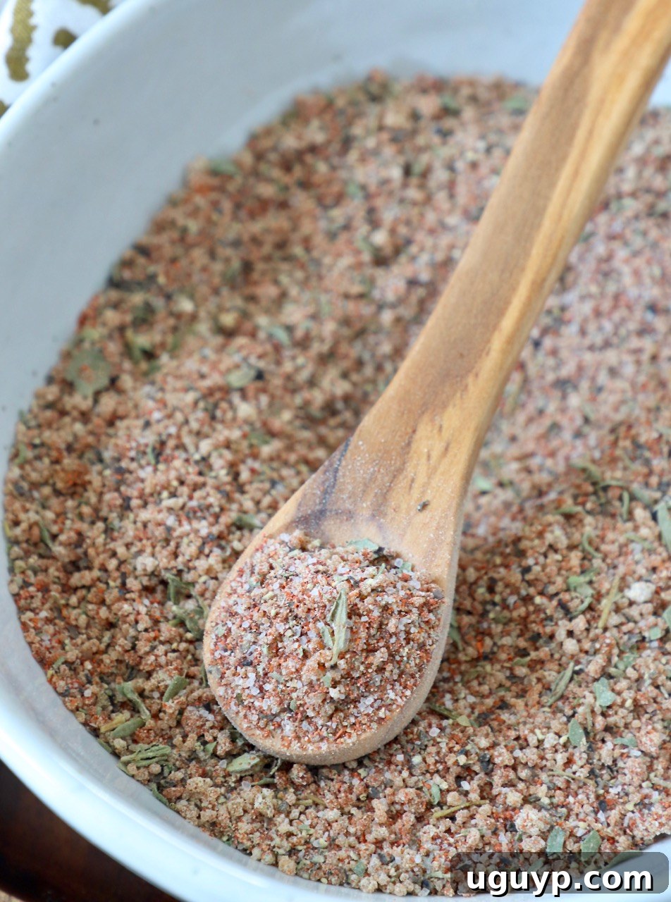 A close-up of the brown sugar pork chop seasoning blend in a clear bowl with a wooden spoon, showcasing its rich texture.