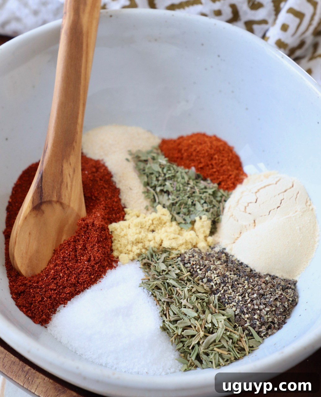 A vibrant collection of spices and herbs in a white bowl with a wooden spoon, representing the freshness of homemade seasoning.