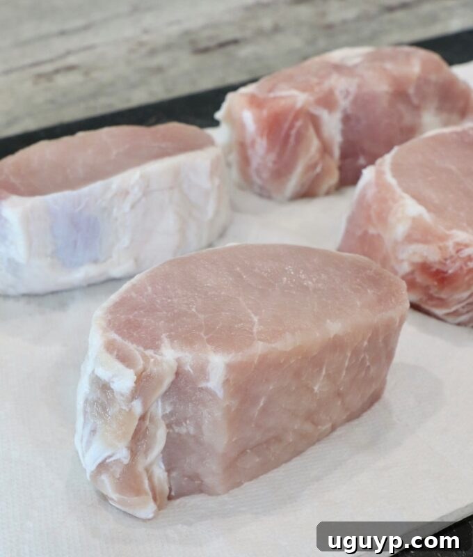 Thick pork chops resting on paper towels on a cutting board, being patted dry after brining.