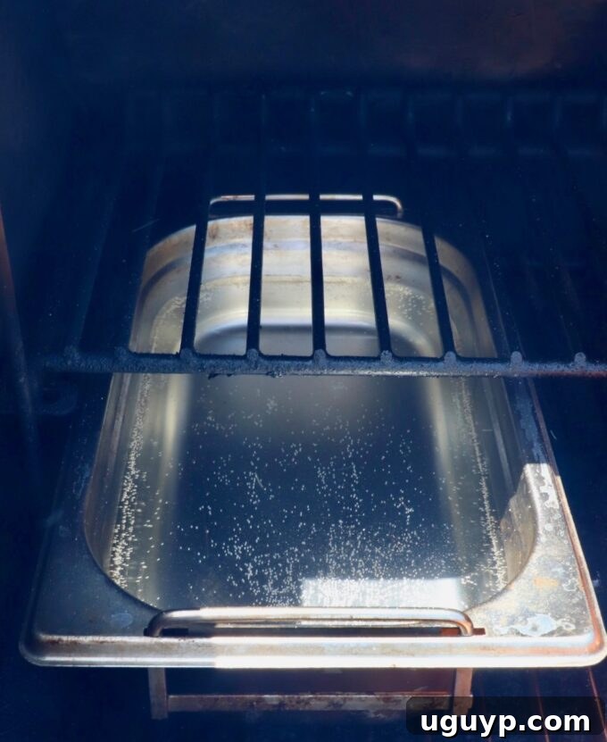 A smoker-safe pan filled with water positioned inside a smoker, ready to maintain moisture during cooking.