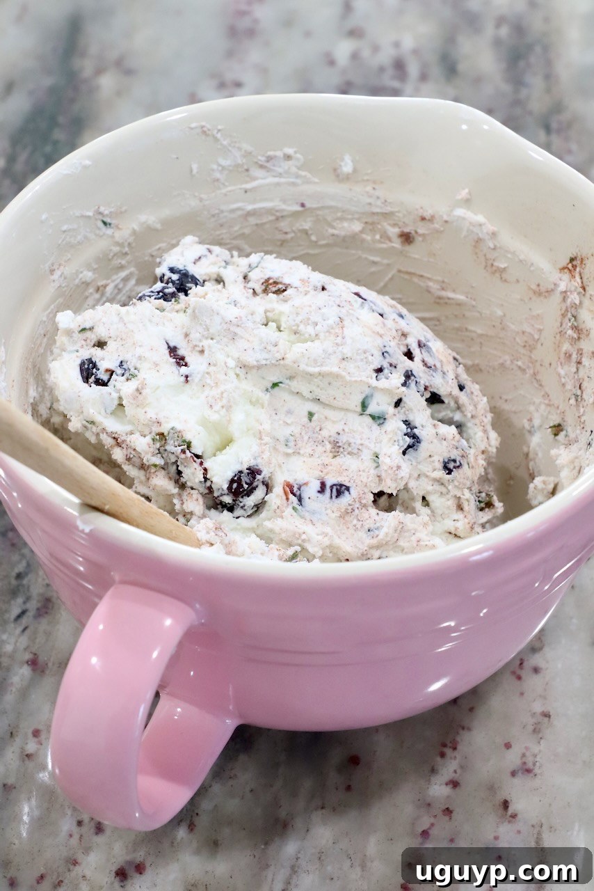 Creamy goat cheese combined with dried cranberries and minced fresh rosemary and cinnamon in a pink ceramic mixing bowl, ready to be spread.