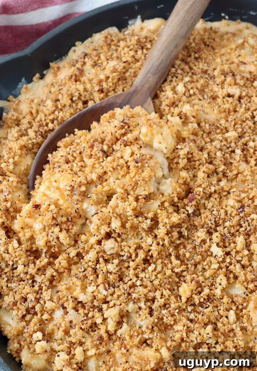 A serving spoon in a skillet of freshly smoked mac and cheese, showing the creamy interior and crispy topping.
