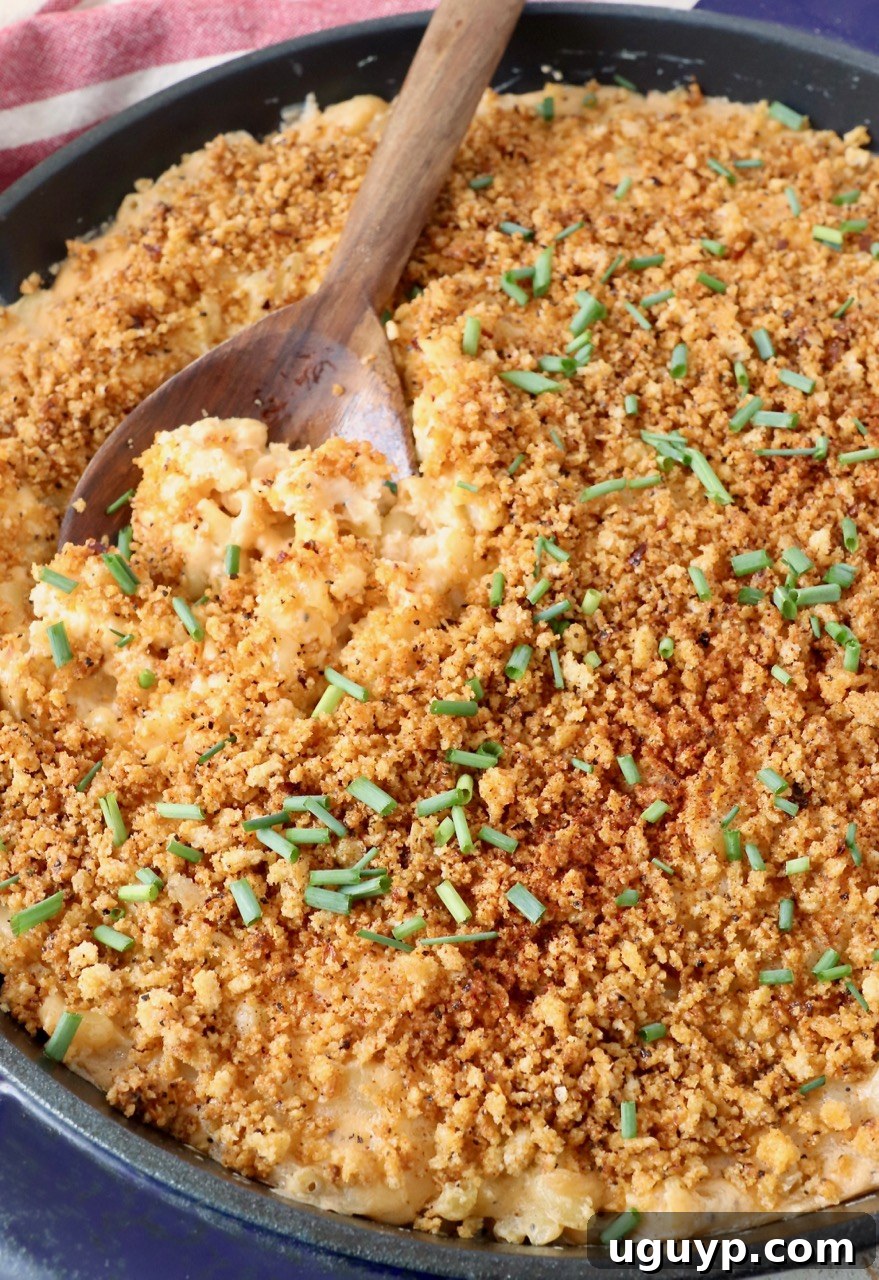 A serving spoon in a skillet of smoked mac and cheese, garnished with fresh chopped chives, highlighting its rich texture.