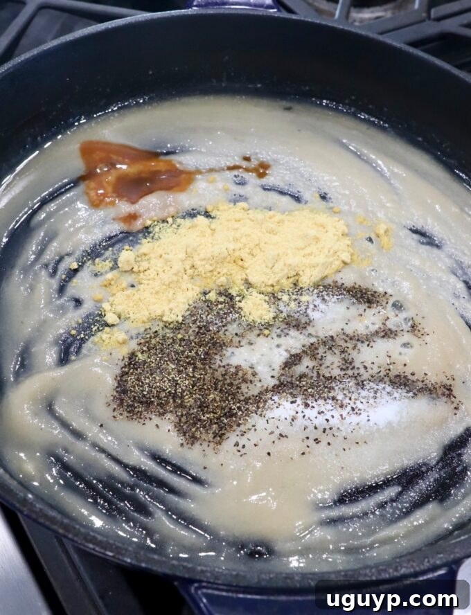 A perfectly smooth roux seasoned with mustard powder, salt, pepper, and a dash of hot sauce in a skillet.