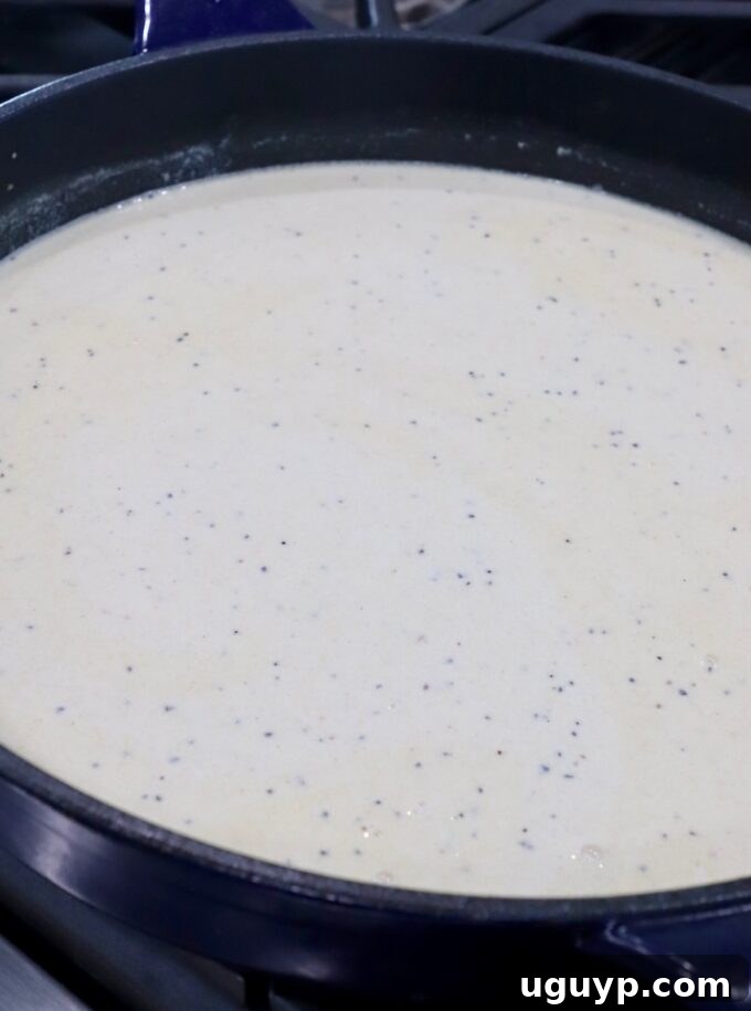 Half and half being slowly poured into the seasoned roux in a skillet, stirring to create a creamy base.