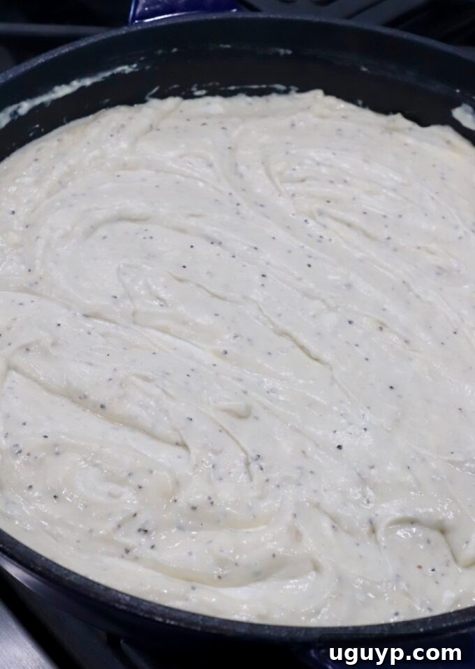 Cubed cream cheese melting into a smooth, simmering sauce in a skillet on the stove.