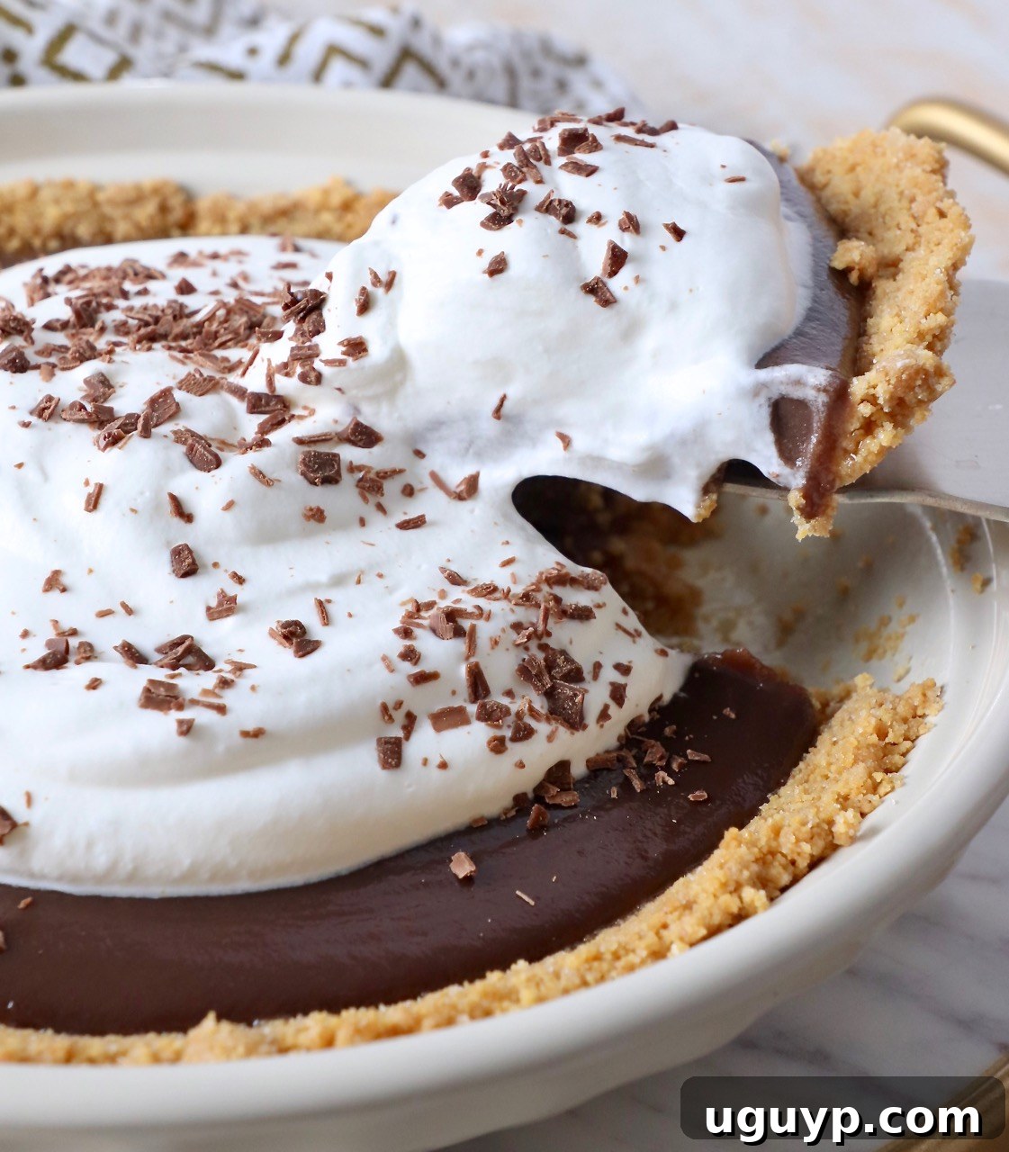 A perfect slice of Meme's Famous Chocolate Pie being lifted from the pie dish, showcasing its rich chocolate filling and generous whipped cream topping.