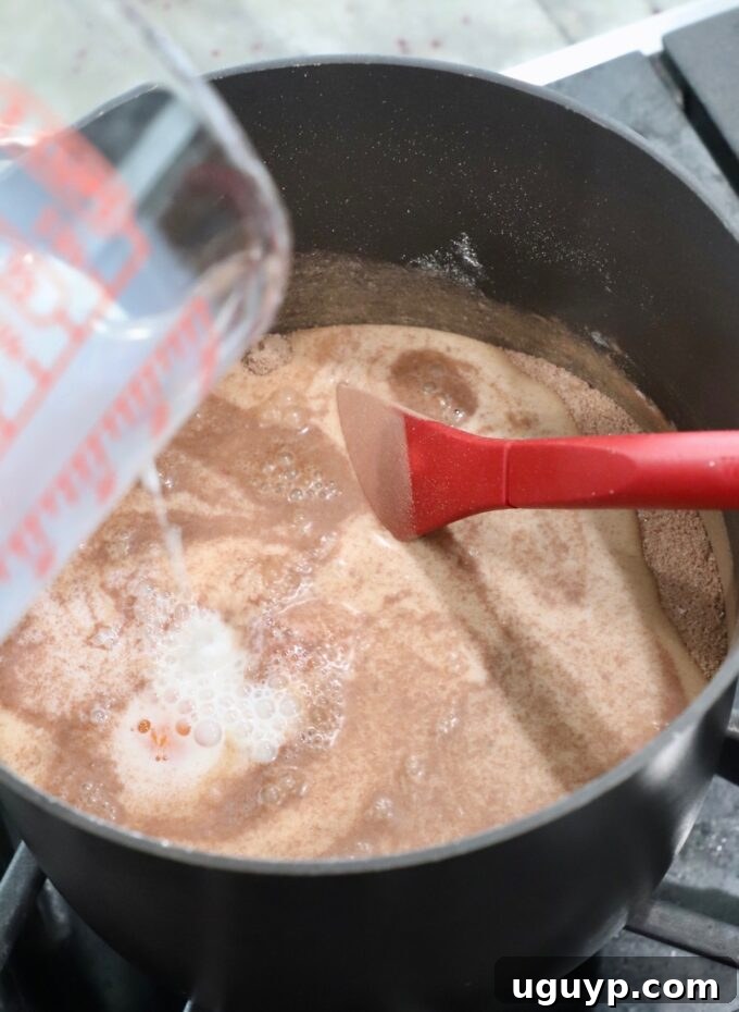 Milk being poured into the saucepan with the dry ingredients and whisked egg yolks, beginning the chocolate pie filling mixture.