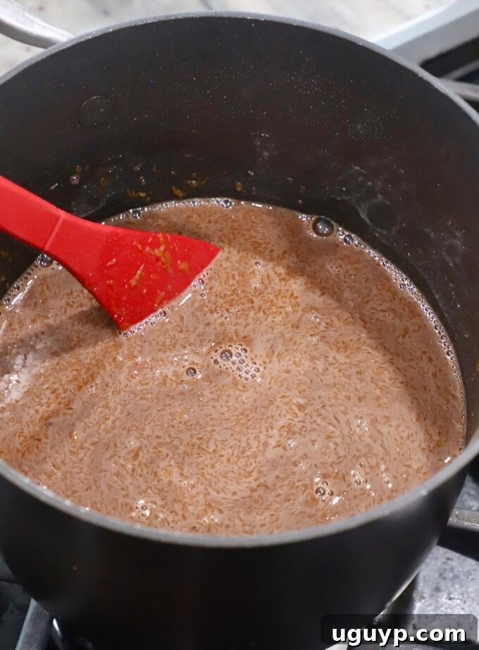 A red spoon continuously stirring the chocolate pie filling in a saucepan over medium heat as it begins to thicken.