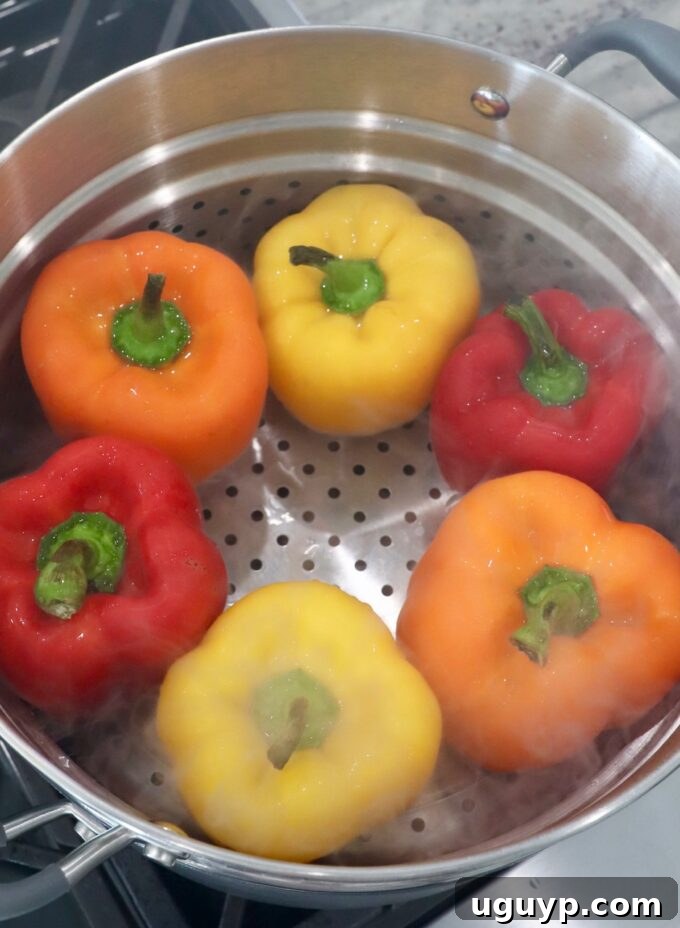 Bell peppers arranged neatly in a steamer basket over boiling water on the stove, preparing them for stuffing.