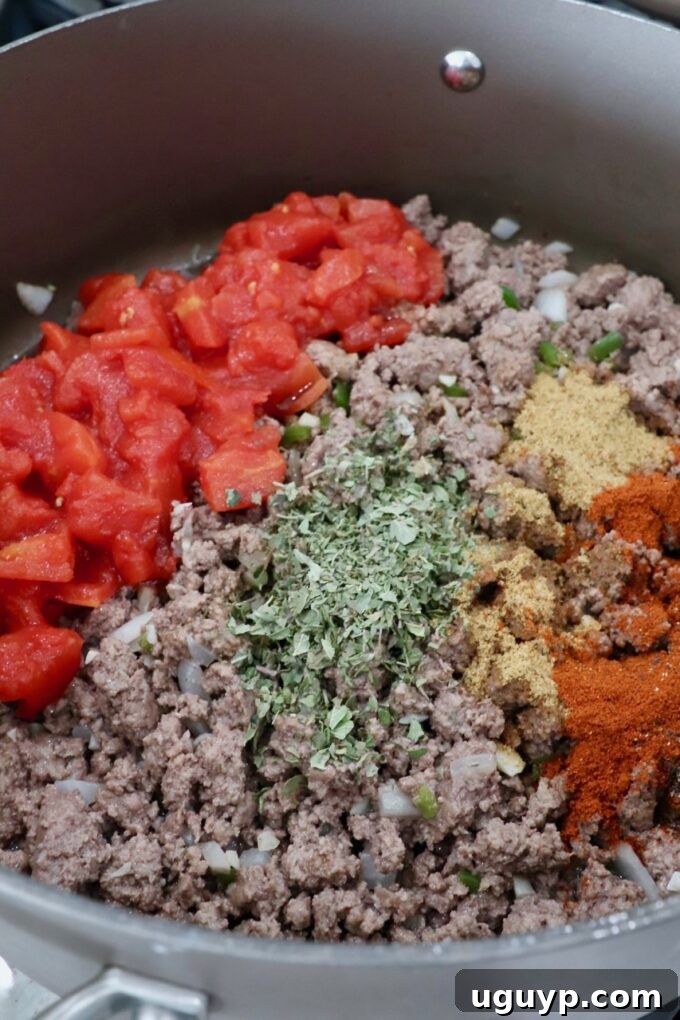 Cooked ground beef mixture simmering in a skillet with diced tomatoes, Worcestershire sauce, oregano, beef bouillon, paprika, and black pepper, creating a rich filling.