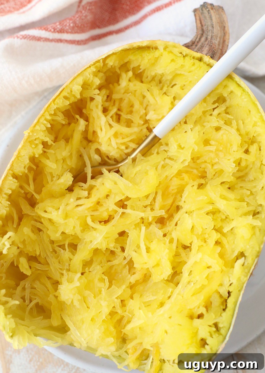 A half of microwaved spaghetti squash on a plate, with a fork ready to shred the strands.