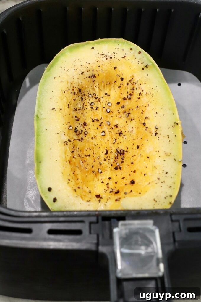 An uncooked spaghetti squash half placed cut-side up in an air fryer basket, ready for cooking.