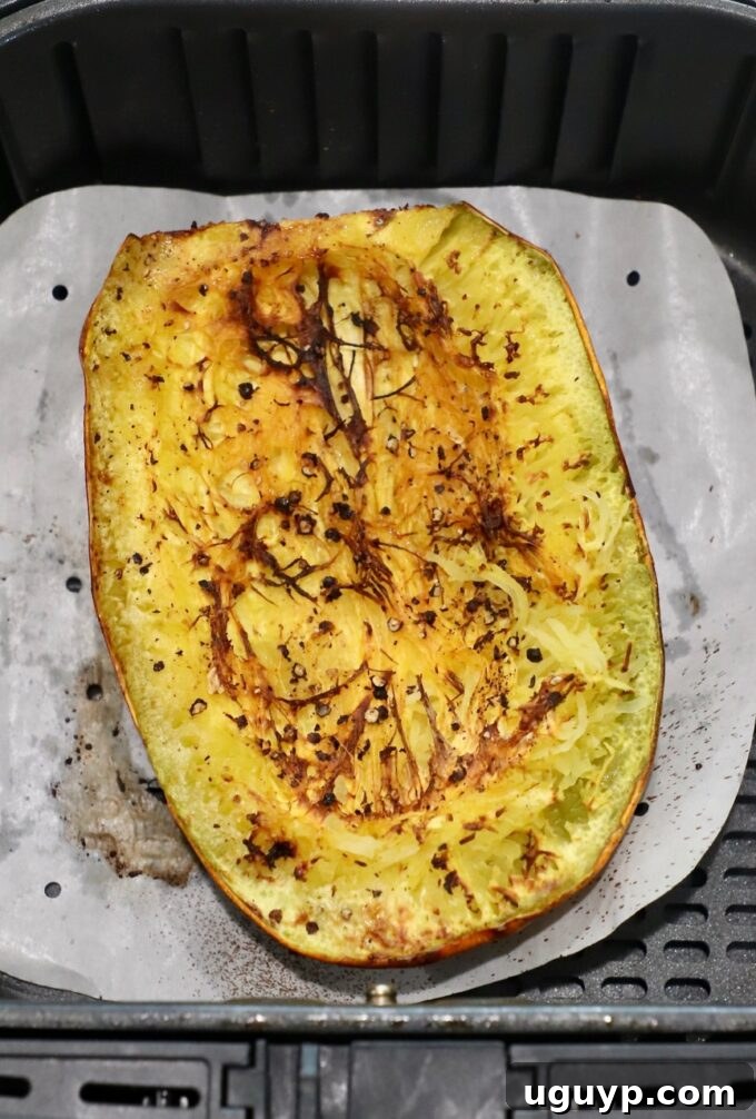 A cooked spaghetti squash half in an air fryer basket, showing slightly browned and tender flesh.