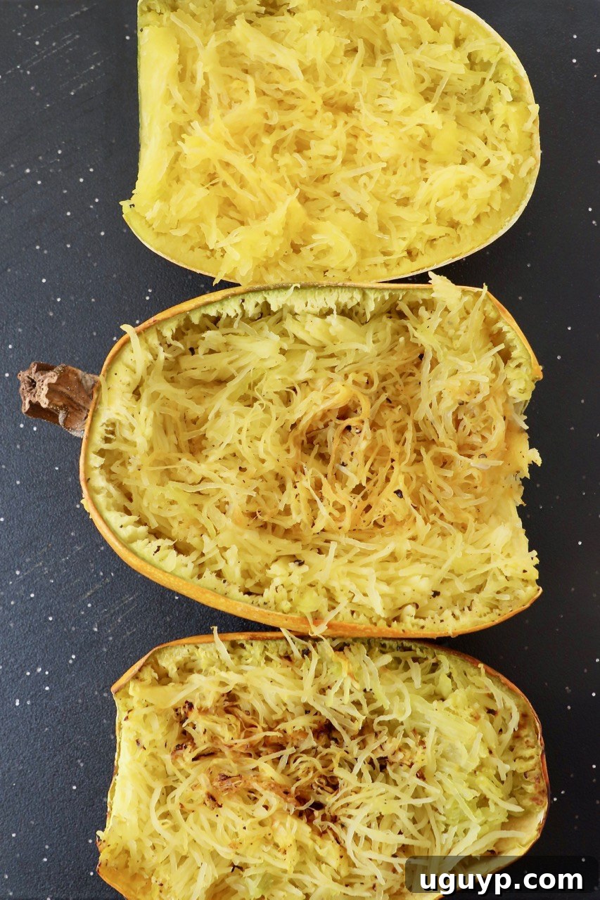Three halves of cooked spaghetti squash, some showing golden-brown edges, on a cutting board.