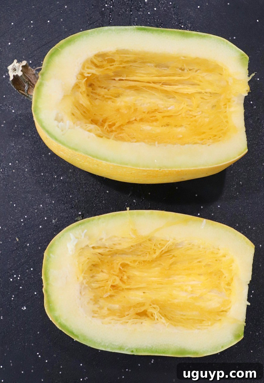 A spaghetti squash sliced in half on a wooden cutting board, showcasing its raw interior and seeds.